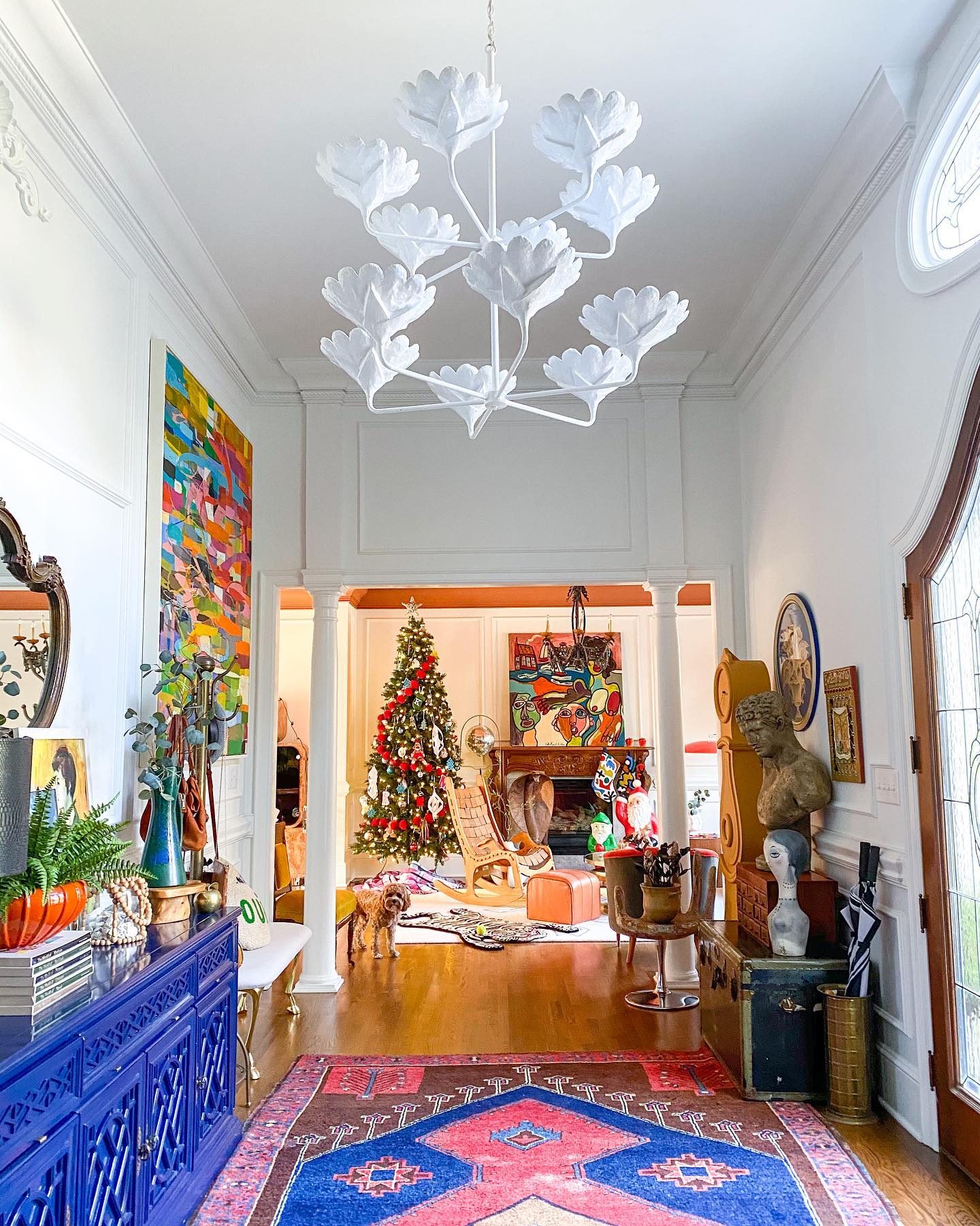 Large entryway chandelier light with royal blue credenza and pink and blue rug