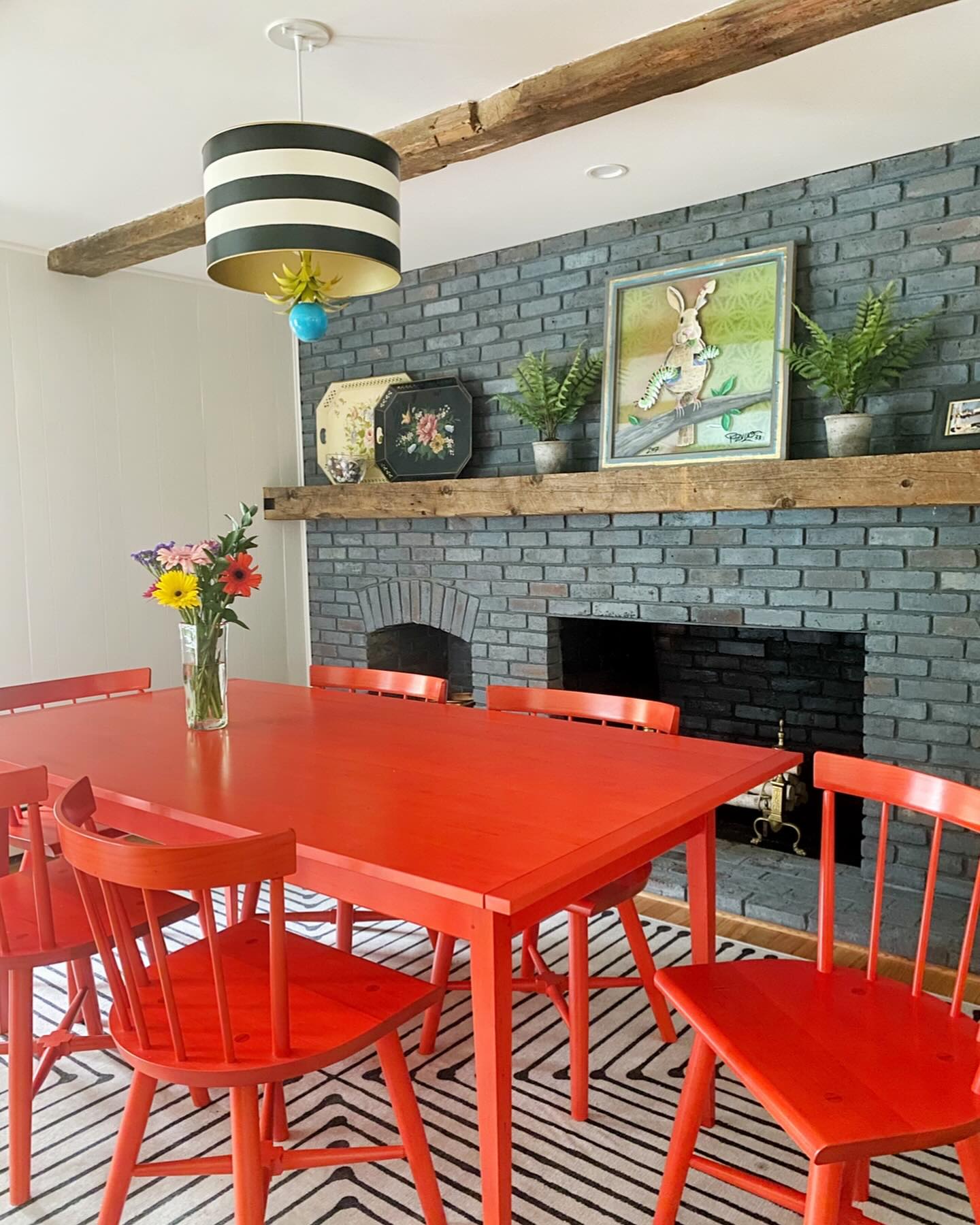 pendant light for dining room over a bright red kitchen table next to a firepplace with mantel decorations